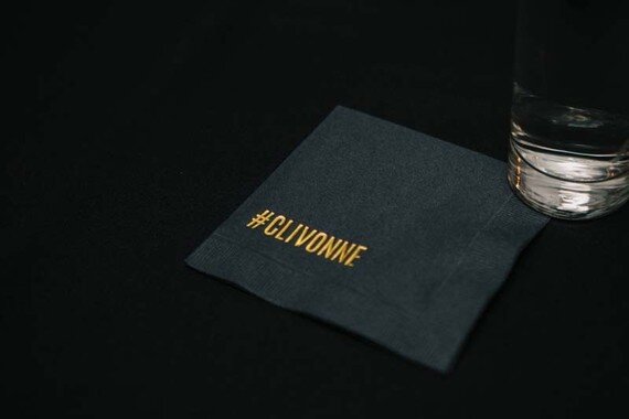 A black cocktail napkin with the couple's hashtag