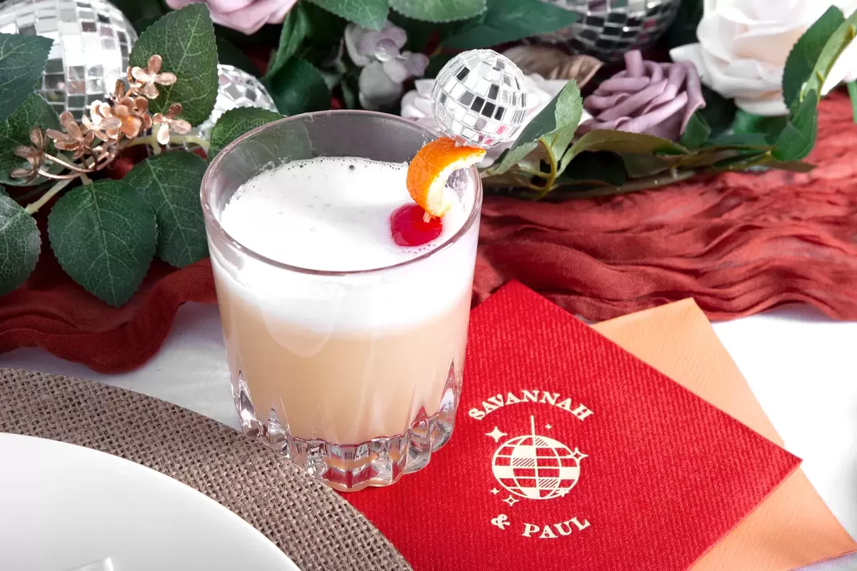 Hand placing garnishes in an egg white whiskey sour.