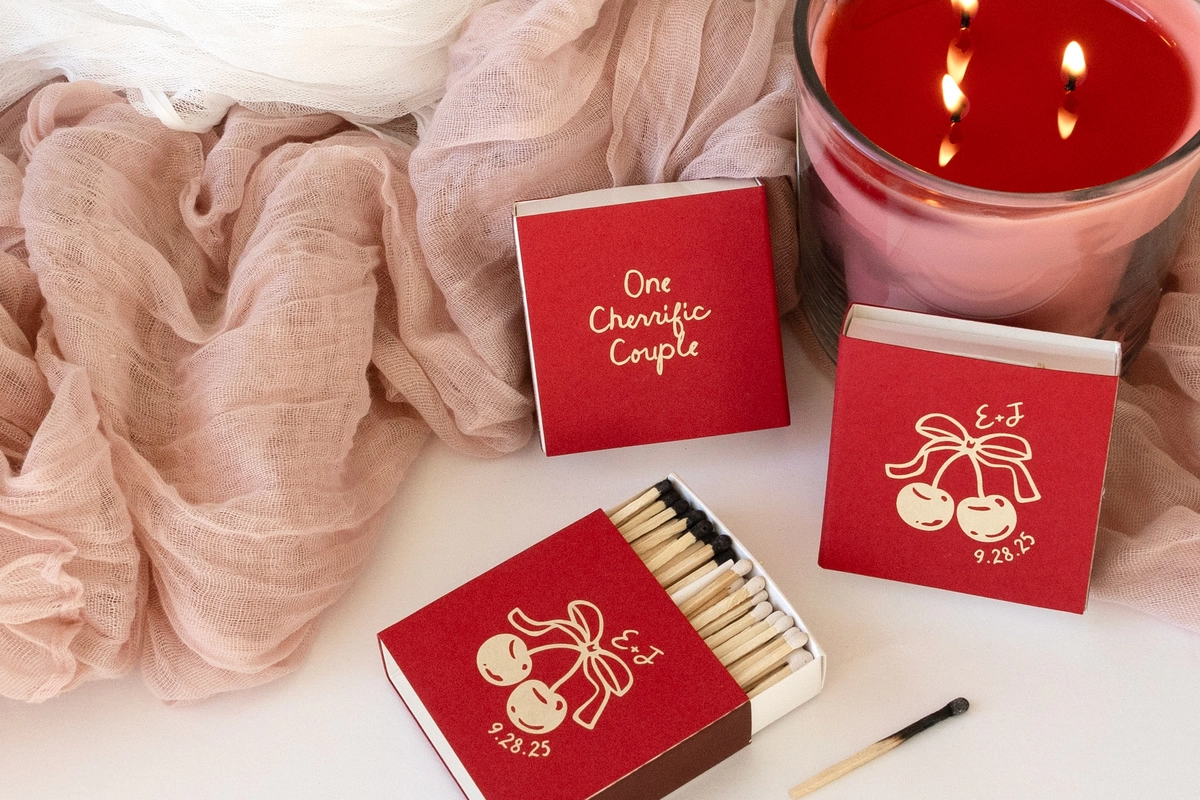 3 Large Red Matchboxes next to a lit candle with a cherry graphic on them 