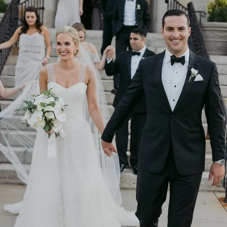 couple wearing black tie holding hands in front of a staircase.