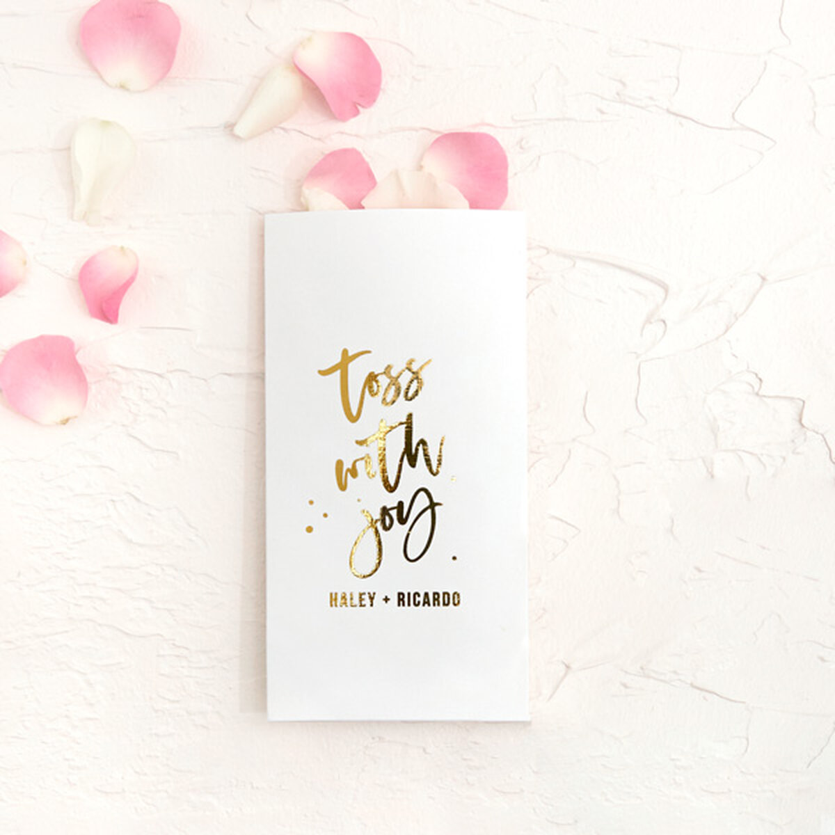 Party pocket white with shiny gold foil stamped "toss with joy" design stuffed with pink and white flower petals