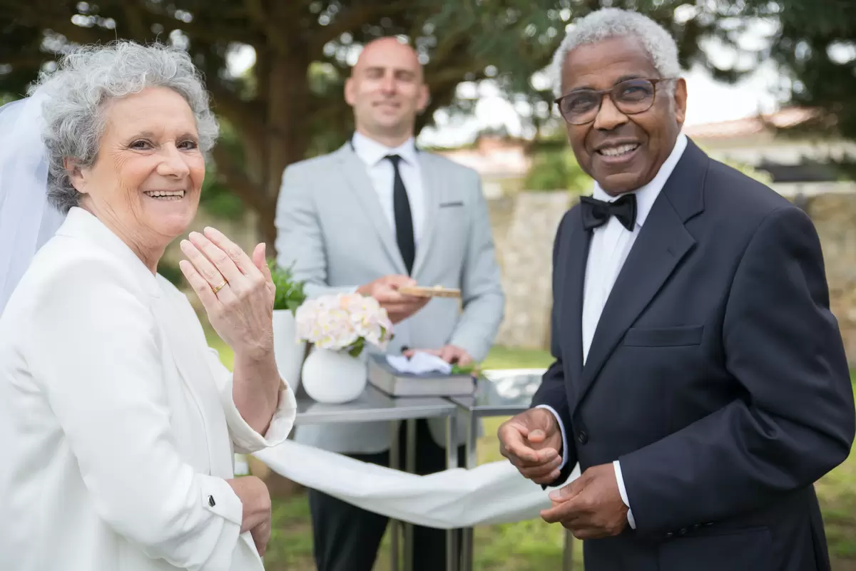 a woman and man getting married in black tie, the woman has her hand raised to show off her wedding ring.