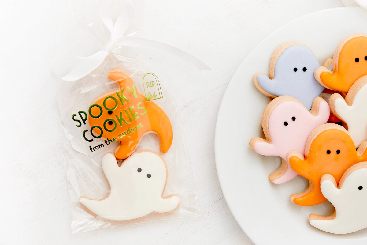Ghost shaped cookies with pastel frosting. One placed in a clear cellophane bag that says "Spooky Cookies".