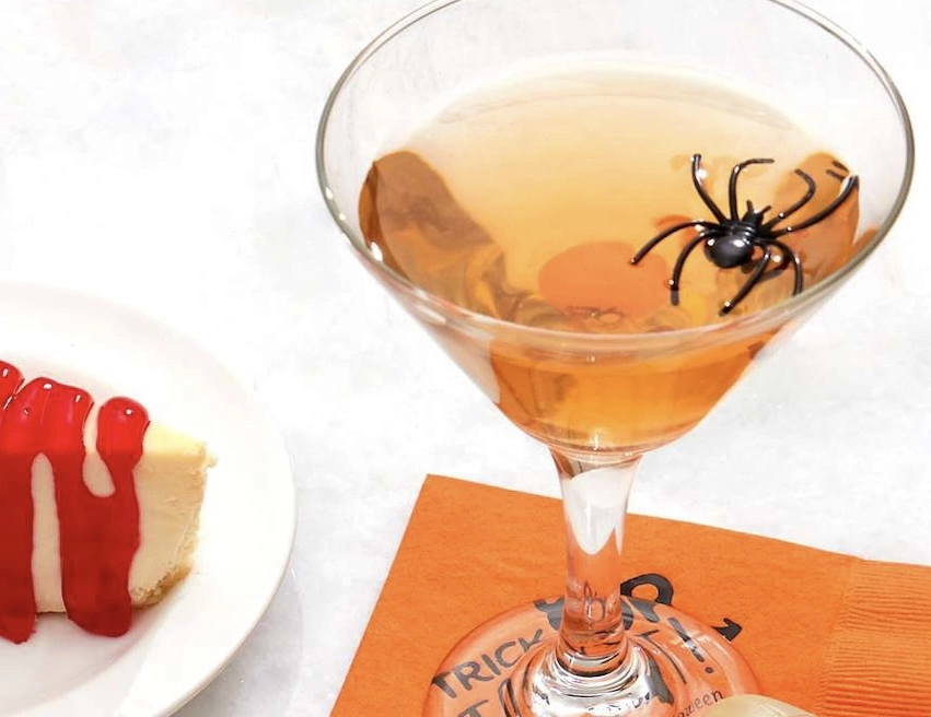 Candy Corn Martini with plastic spider in drink. Martini glass is on top of an orange napkin. 