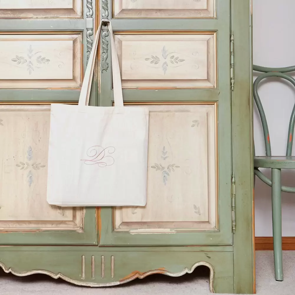 Customized tote bag with pink script hanging from green cupboard