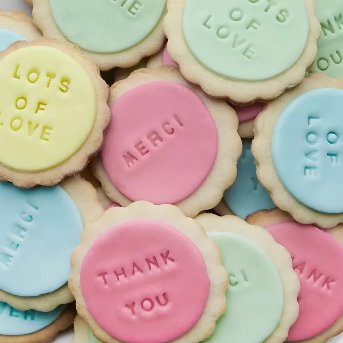 Pile of sugar cookies with fondant on them and phrases stamped into the fondant
